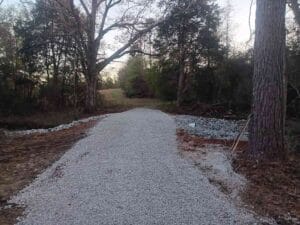 A gravel road extends through a wooded area with trees on both sides and a clearing visible in the distance.